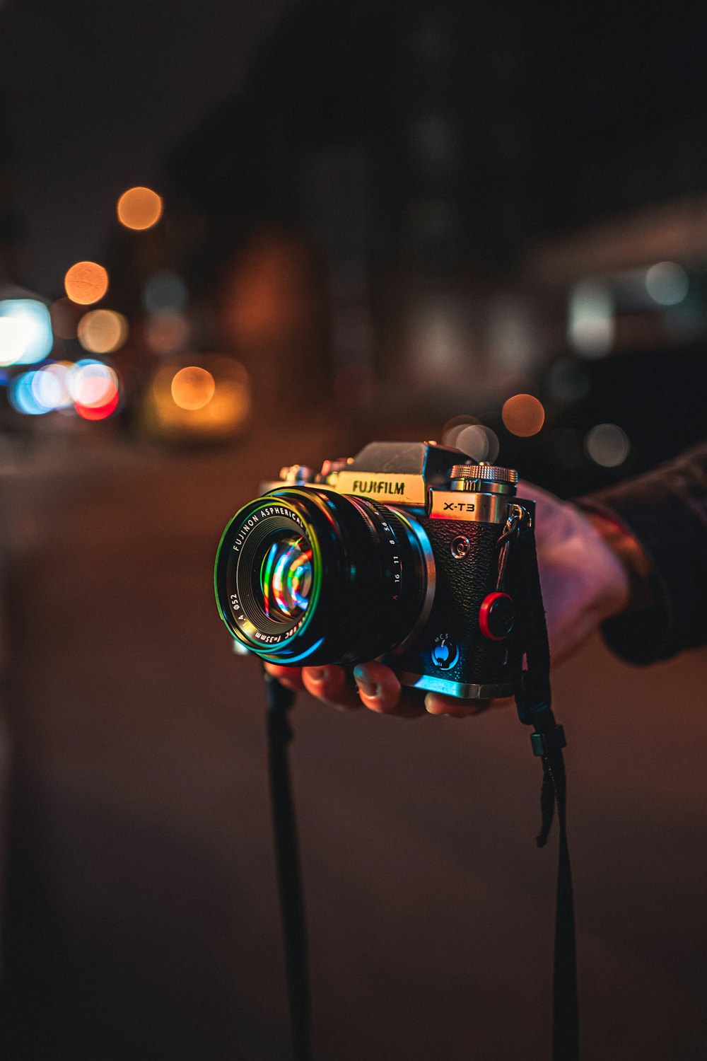 Fujifilm X-T3 mirrorless camera held against a moody night street with warm bokeh